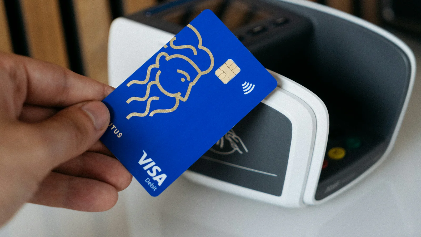 Hand holding a blue Visa debit card at a contactless payment terminal
