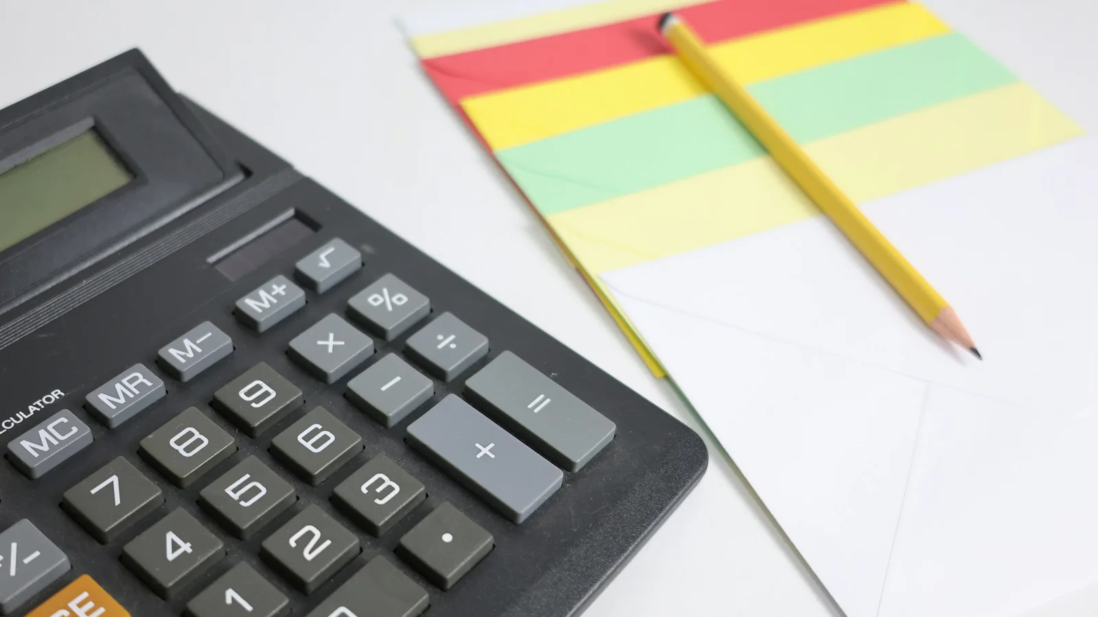 Calculator, pencil, and colorful notepad on a clean desk